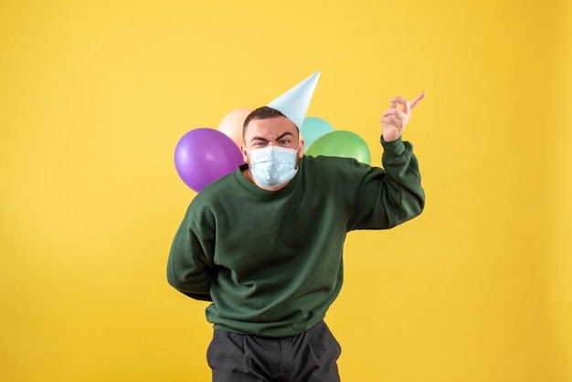 Junges Männchen der Vorderansicht, das bunte Ballons auf gelbem Hintergrund hält