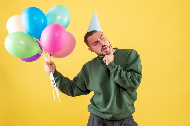 Junges Männchen der Vorderansicht, das bunte Ballons auf gelbem Hintergrund hält