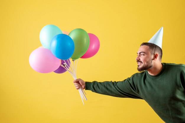 Junges Männchen der Vorderansicht, das bunte Ballons auf gelbem Hintergrund hält