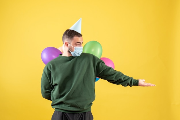 Junges männchen der vorderansicht, das bunte ballons auf gelbem hintergrund hält