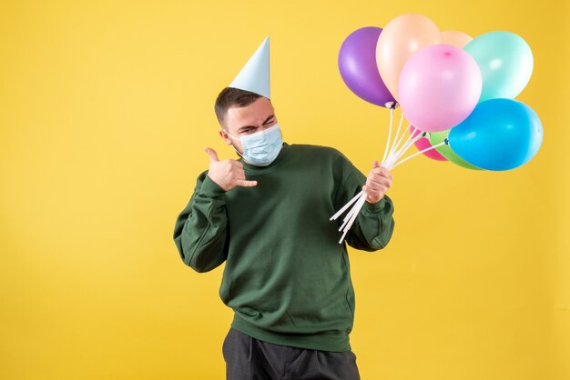 Junges Männchen der Vorderansicht, das bunte Ballons auf gelbem Hintergrund hält