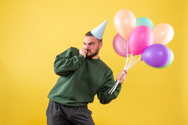 Junges Männchen der Vorderansicht, das bunte Ballons auf gelbem Hintergrund hält