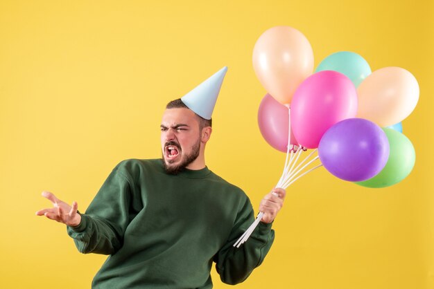 Junges Männchen der Vorderansicht, das bunte Ballons auf gelbem Hintergrund hält