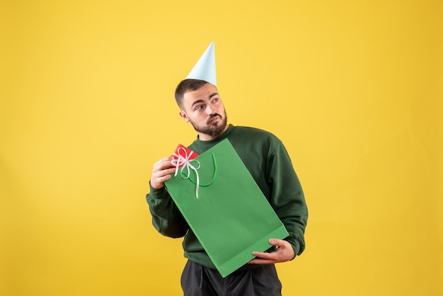 Junges männchen der vorderansicht, das kleines geschenk auf gelbem hintergrund hält