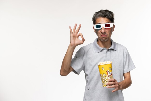 Junges Männchen der Vorderansicht, das Popcorn in d Sonnenbrille auf einer hellen weißen Oberfläche hält