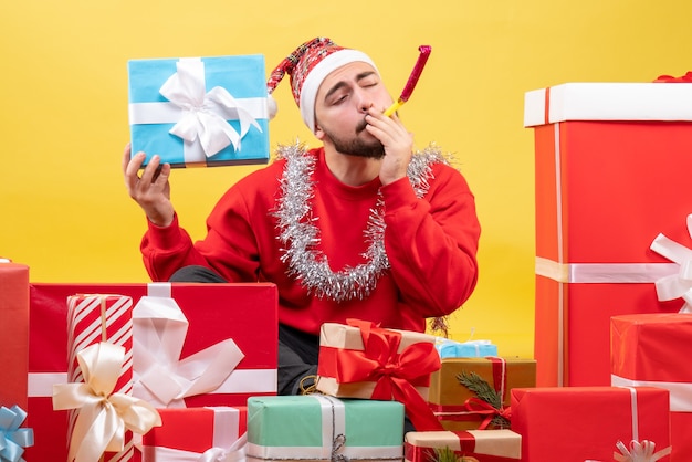 Kostenloses Foto junges männchen der vorderansicht, das um weihnachtsgeschenke auf gelbem hintergrund sitzt