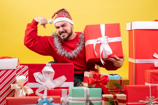 Junges Männchen der Vorderansicht, das um Weihnachtsgeschenke auf gelbem Hintergrund sitzt