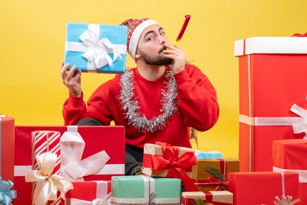 Junges Männchen der Vorderansicht, das um Weihnachtsgeschenke auf gelbem Hintergrund sitzt