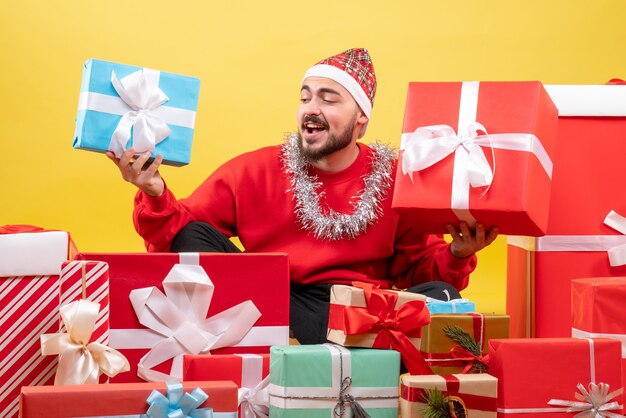 Junges Männchen der Vorderansicht, das um Weihnachtsgeschenke auf gelbem Hintergrund sitzt