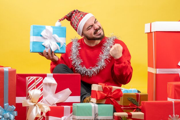 Junges Männchen der Vorderansicht, das um Weihnachtsgeschenke auf gelbem Hintergrund sitzt