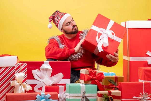Junges Männchen der Vorderansicht, das um Weihnachtsgeschenke auf gelbem Hintergrund sitzt