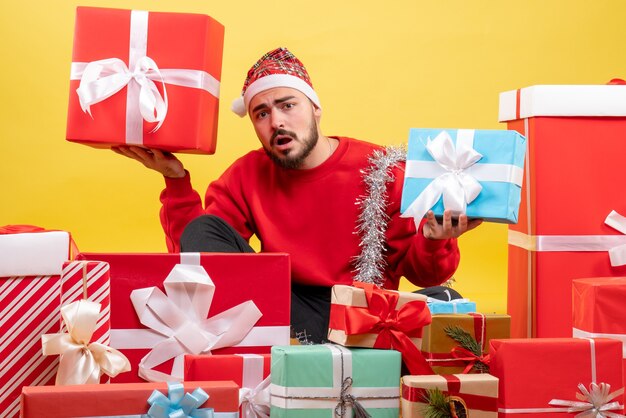 Junges Männchen der Vorderansicht, das um Weihnachtsgeschenke auf gelbem Hintergrund sitzt