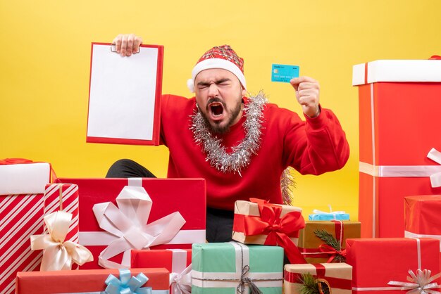 Junges Männchen der Vorderansicht, das um Weihnachtsgeschenke auf gelbem Hintergrund sitzt