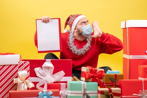 Junges Männchen der Vorderansicht, das um Weihnachtsgeschenke auf gelbem Hintergrund sitzt