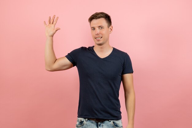 Junges Männchen der Vorderansicht im blauen T-Shirt, das seine Handfläche auf dem männlichen menschlichen Emotionsfarbmodell des rosa Hintergrunds zeigt