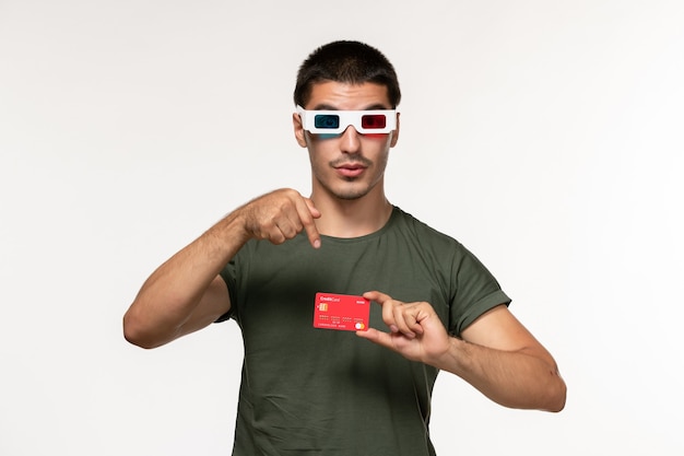 Junges Männchen der Vorderansicht im grünen T-Shirt, das Bankkarte auf einsamem Kino des weißen Wandfilms hält