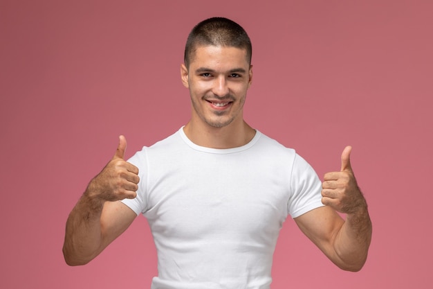 Junges Männchen der Vorderansicht im weißen T-Shirt, das zeigt, wie Zeichen auf rosa Hintergrund zeigt