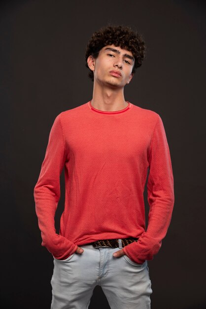 Junges Modell im roten Hemd, das durch das Aufstellen der Hände auf seinen Taschen aufwirft.