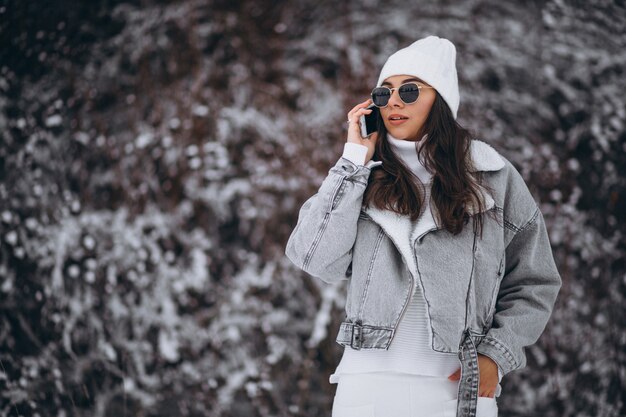 Junges modisches Mädchen in einem Winterpark unter Verwendung des Telefons