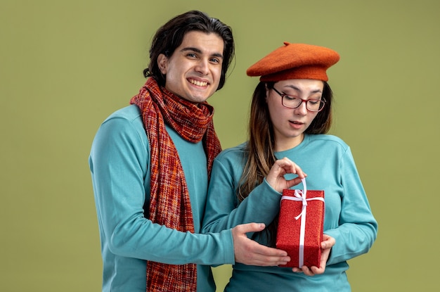 Junges Paar am Valentinstag Kerl mit Schal Mädchen mit Hut Mädchen mit Geschenkbox isoliert auf olivgrünem Hintergrund