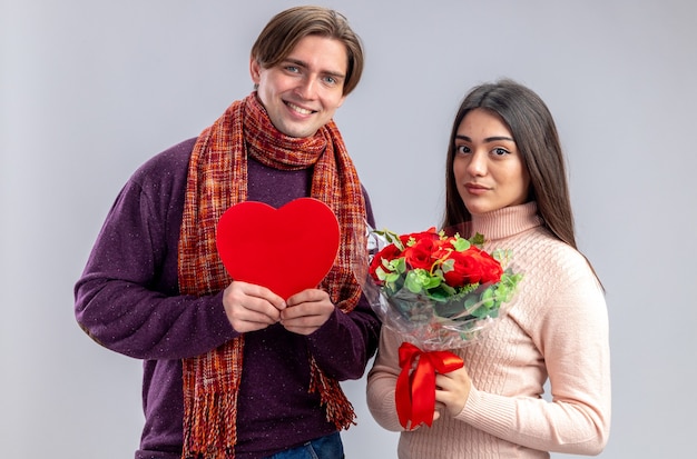 Junges Paar am Valentinstag lächelnder Kerl mit herzförmigem Kasten erfreutes Mädchen mit Blumenstrauß isoliert auf weißem Hintergrund