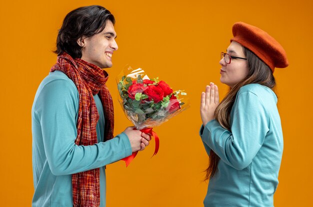 Junges Paar am Valentinstag lächelnder Kerl mit Schal, der dem Mädchen Blumenstrauß auf orangem Hintergrund gibt