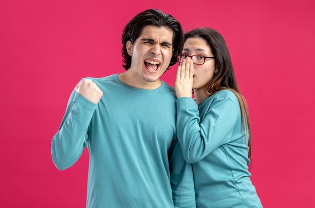 Junges Paar am Valentinstag Mädchen flüstert Kerl mit Ja-Geste isoliert auf rosa Hintergrund