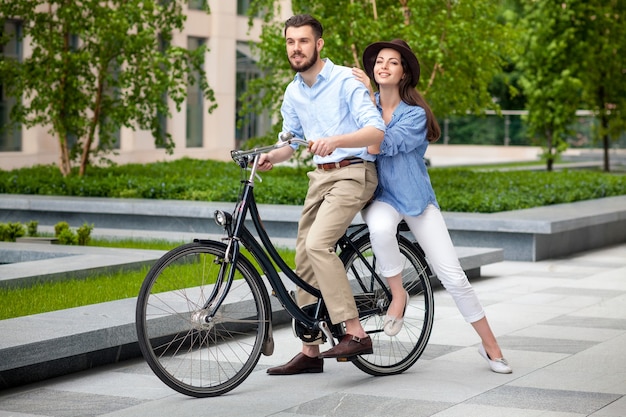 Junges Paar, das auf einem Fahrrad gegenüber dem grünen Stadtpark sitzt