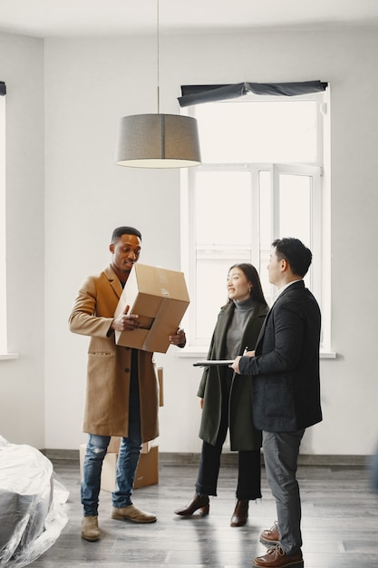 Junges Paar, das ein neues Haus kauft. Asiatische Frau und afrikanischer Mann. Unterschreiben von Dokumenten im neuen Zuhause.