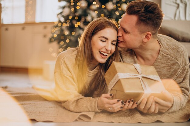 Junges Paar, das einander durch den Weihnachtsbaum Geschenke macht