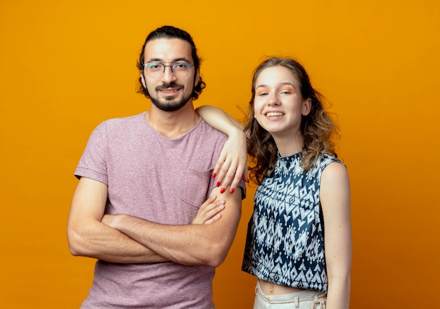 Junges Paar, das Kamera betrachtet, die glücklich und positiv über orange Hintergrund lächelt