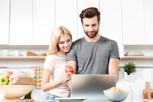 Junges Paar, das Laptop verwendet, um Rezept für ihre Mahlzeit nachzuschlagen