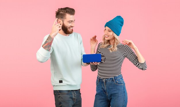 Junges Paar, das Musik auf drahtlosem Lautsprecher hört, der kühles stilvolles Outfit trägt, das lächelnd auf Rosa aufwirft