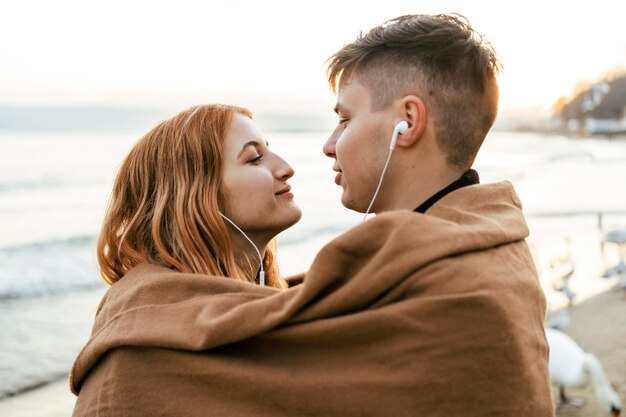 Junges Paar, das Musik auf Kopfhörern am Strand im Winter hört