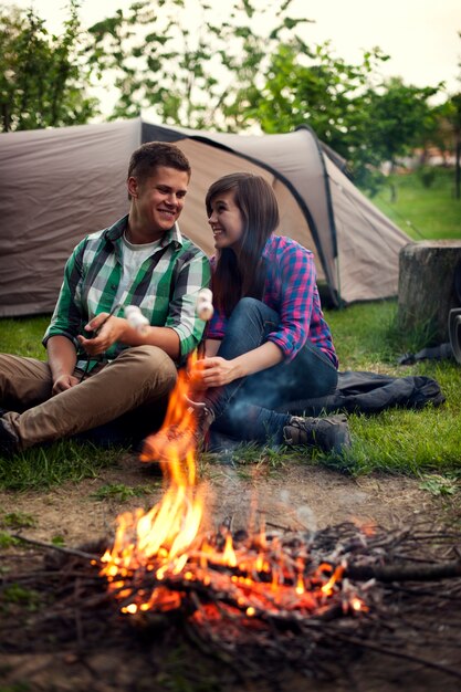 Junges Paar, das nahe einem Lagerfeuer sitzt und Marshmallow röstet