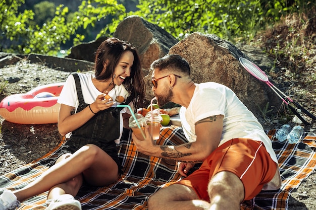 Junges Paar, das Picknick am Flussufer im sonnigen Tag hat