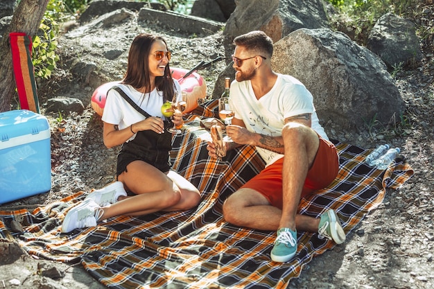 Junges Paar, das Picknick am Flussufer im sonnigen Tag hat