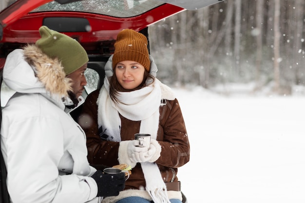 Junges Paar, das während eines Winter-Roadtrips warme Getränke und ein Sandwich genießt