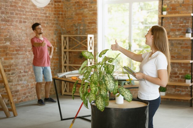 Junges Paar, das zusammen Wohnungsreparatur macht. Verheirateter Mann und Frau machen Renovierung oder Renovierung zu Hause. Konzept der Beziehungen, Familie, Liebe. Überprüfen Sie das fertige Design und stellen Sie neue Möbel auf.