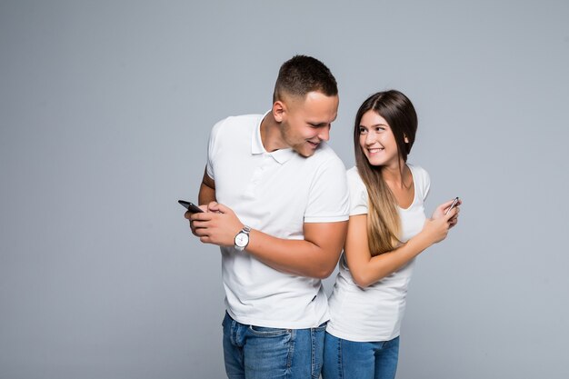 Junges Paar der Männer und der Frau, die mit Handys in ihren Händen lokalisiert auf grauem Hintergrund stehen