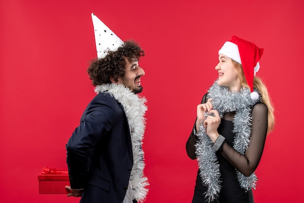 Junges Paar der Vorderansicht, das Feiertagsgeschenke auf der roten Wand-Emotionsliebesweihnachten austauscht