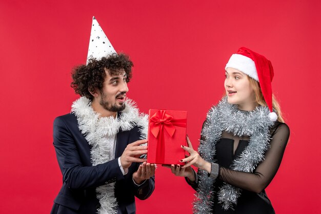 Junges Paar der Vorderansicht, das Neujahrsgeschenk auf der roten Wand Emotion Weihnachtsliebe hält