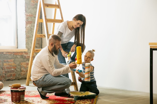 Junges Paar, Familie, die zusammen Wohnungsreparatur macht. Mutter, Vater und Sohn machen Renovierungsarbeiten oder Renovierungen. Konzept der Beziehungen, Bewegung, Liebe. Wand für Tapete vorbereiten