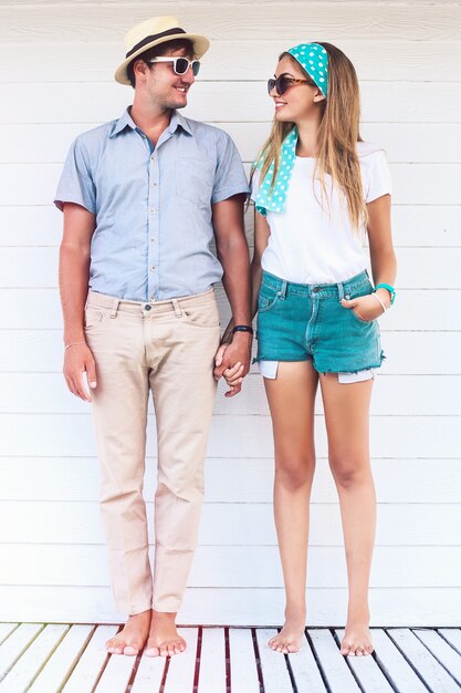 Junges Paar in der Liebe, die nahes weißes Strandcafé im Sommer Retro helle Outfits aufstellt, Hände hält