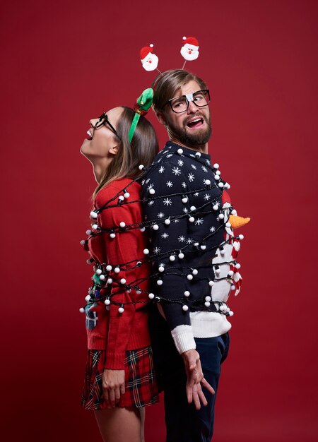 Junges Paar in seltsamen Weihnachtskleidern mit Weihnachtslichtern gebunden