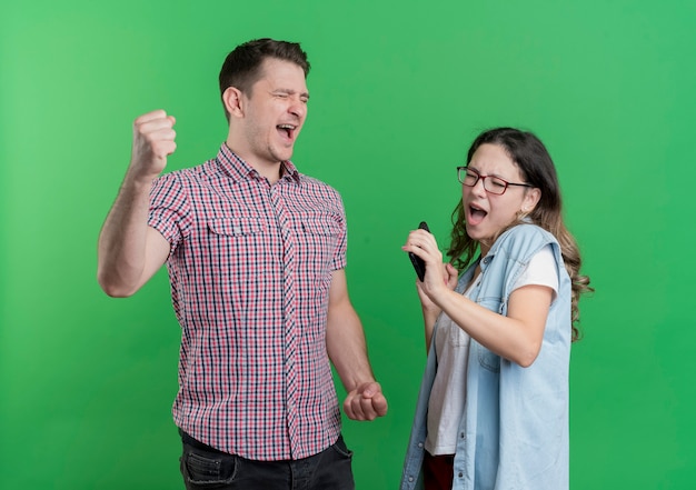 Junges Paar Mann und Frau in Freizeitkleidung glücklich und aufgeregt geballte Fäuste, die über grüner Wand stehen