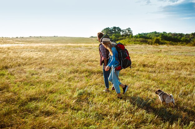 Junges Paar Reisende, die in Feld mit Mops Hund gehen