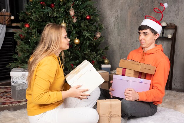 Junges Paar sitzt auf dem Boden mit Geschenken in der Nähe von Weihnachtsbaum