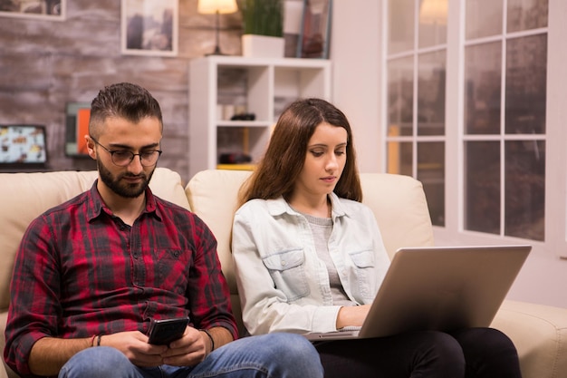 Junges Paar sitzt auf dem Sofa und macht Online-Shopping mit Laptop und Telefon. Freundin, die auf Laptop surft.