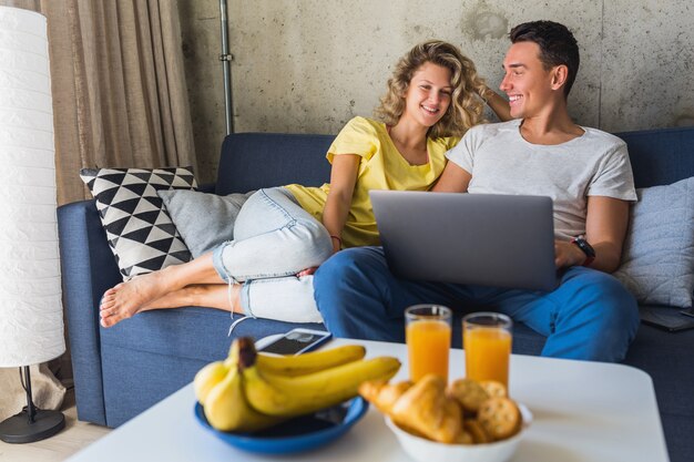 Junges Paar sitzt auf Sofa zu Hause und schaut in Laptop